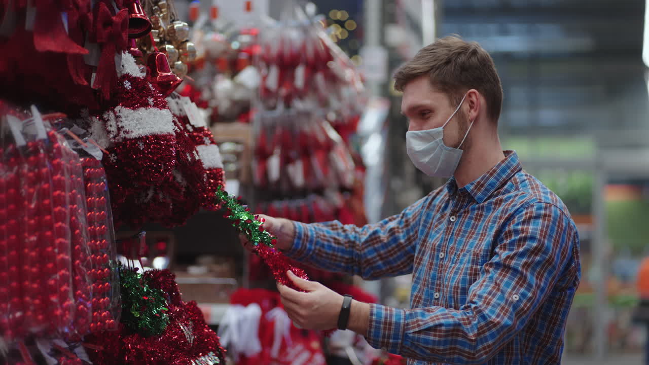 un hombre con una máscara protectora en una joyería y guirnaldas con juguetes para árboles de navidad y en casa. guirnaldas navideñas y decoración