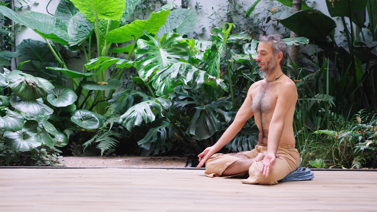Hombre sereno meditando en un suelo de madera rodeado de plantas