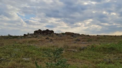 a rocky formation is set against a backdrop of dramatic clouds in a spacious grassland area, as the sun begins to set in the late afternoon