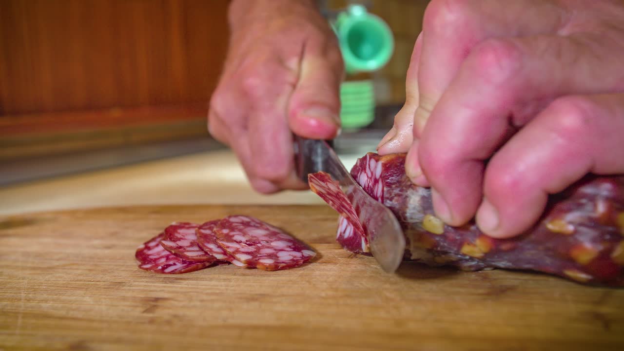 cerrar la mano masculina cortando rodajas finas de salami en una tabla de cortar de madera, tiro estático