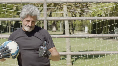vista frontal de un portero senior concentrado atrapando la pelota y luego sonriendo a la cámara