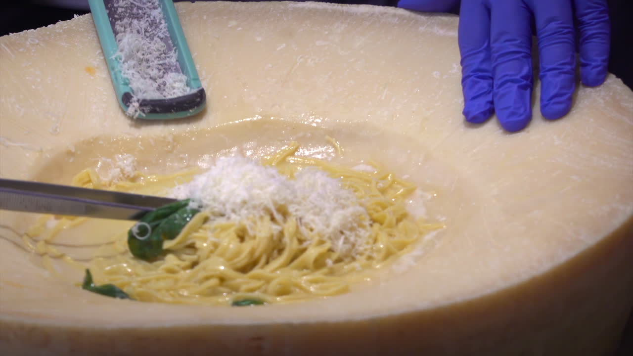 Close up of a waiter scraping parmesan cheese and adding it to the pasta in the wheel