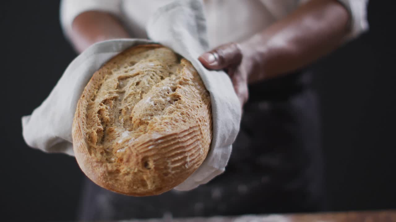 Video of cook holding loaf of bread on black background