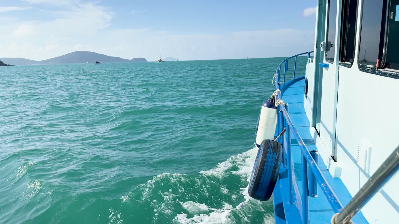 A boat navigates turquoise waters near Phuket, Thailand, using a reused tyre as a fender. Bright daylight enhances the serene ocean view