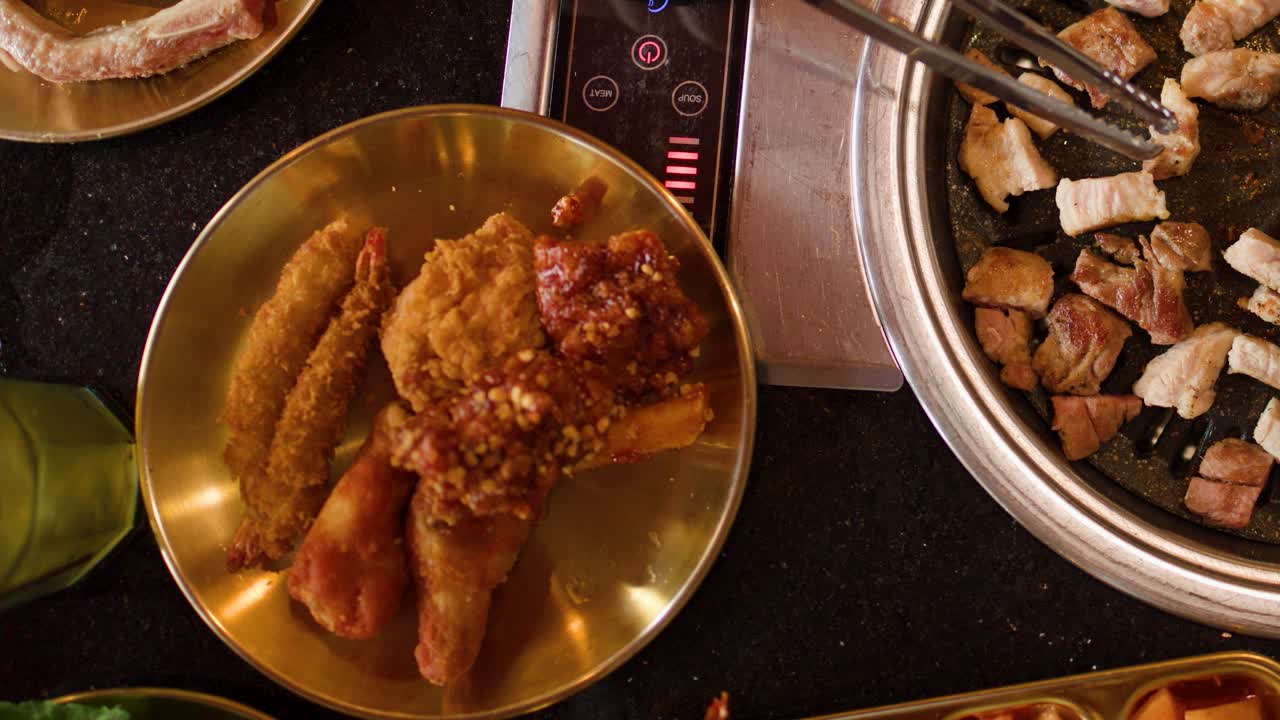 Overhead view of pork belly grilling, tongs turning meat, warm lighting, modern Asian restaurant