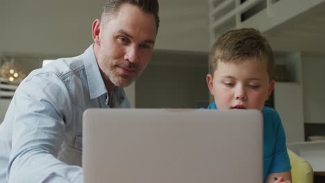 Caucasian-father-with-son-sitting-at-table-and-learning-with-laptop-at-home