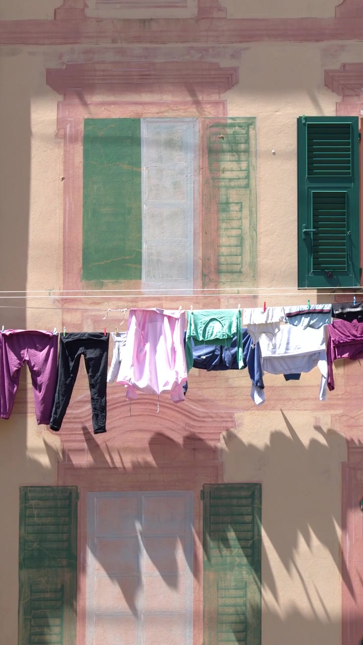 Static shot of colorful laundry drying on a line outside a traditional pink Mediterranean building.