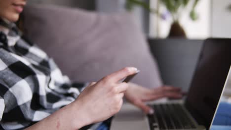 the girl typing numbers from the card to the computer. successfully finished, she continues to type on the laptop. sitting on the couch. at home. move away shooting