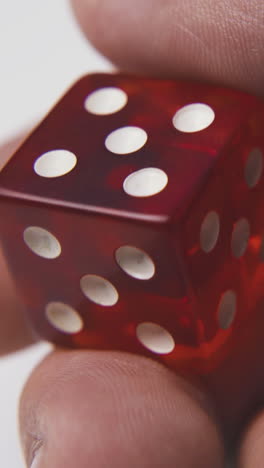 young person shows bright red plastic dices with white spots on sides against light surface extreme close view
