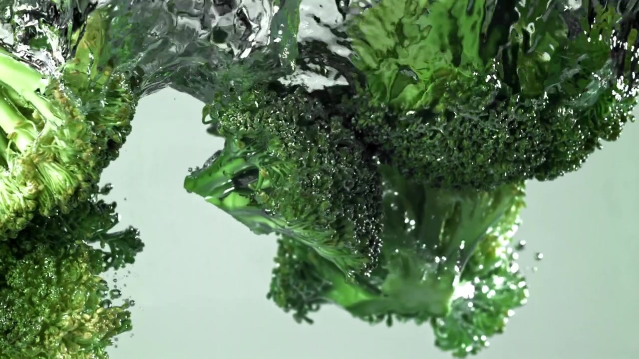 Cimette di broccoli freschi e verdi che cadono in acqua limpida al rallentatore
