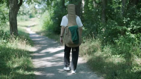 young man walking with guitar on street near forest