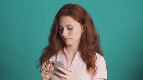 Redheaded girl in front of camera on turquoise background.