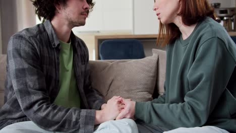 una chica morena con un suéter verde habla de un tema serio sobre las relaciones con su novio una morena con el cabello rizado en una camisa a cuadros sentada en el sofá en un apartamento moderno en casa