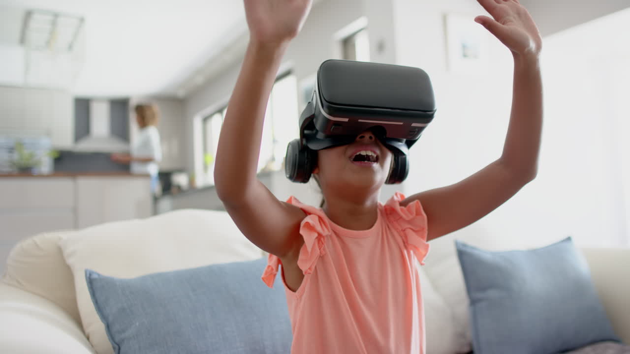 Happy biracial girl wearing vr headset using virtual interface at home, copy space, slow motion