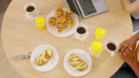 overhead view of a breakfast table with coffee, orange juice, muffins, and avocado toast