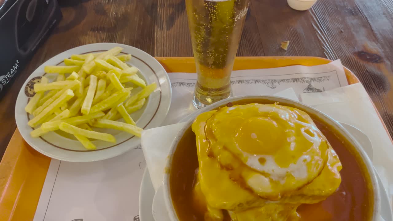 A casual meal with a glass of cold beer, accompanied by fries and a hearty dish with a fried egg on top. The simple comfort food and drink combo is perfect for a laid-back dining experience.