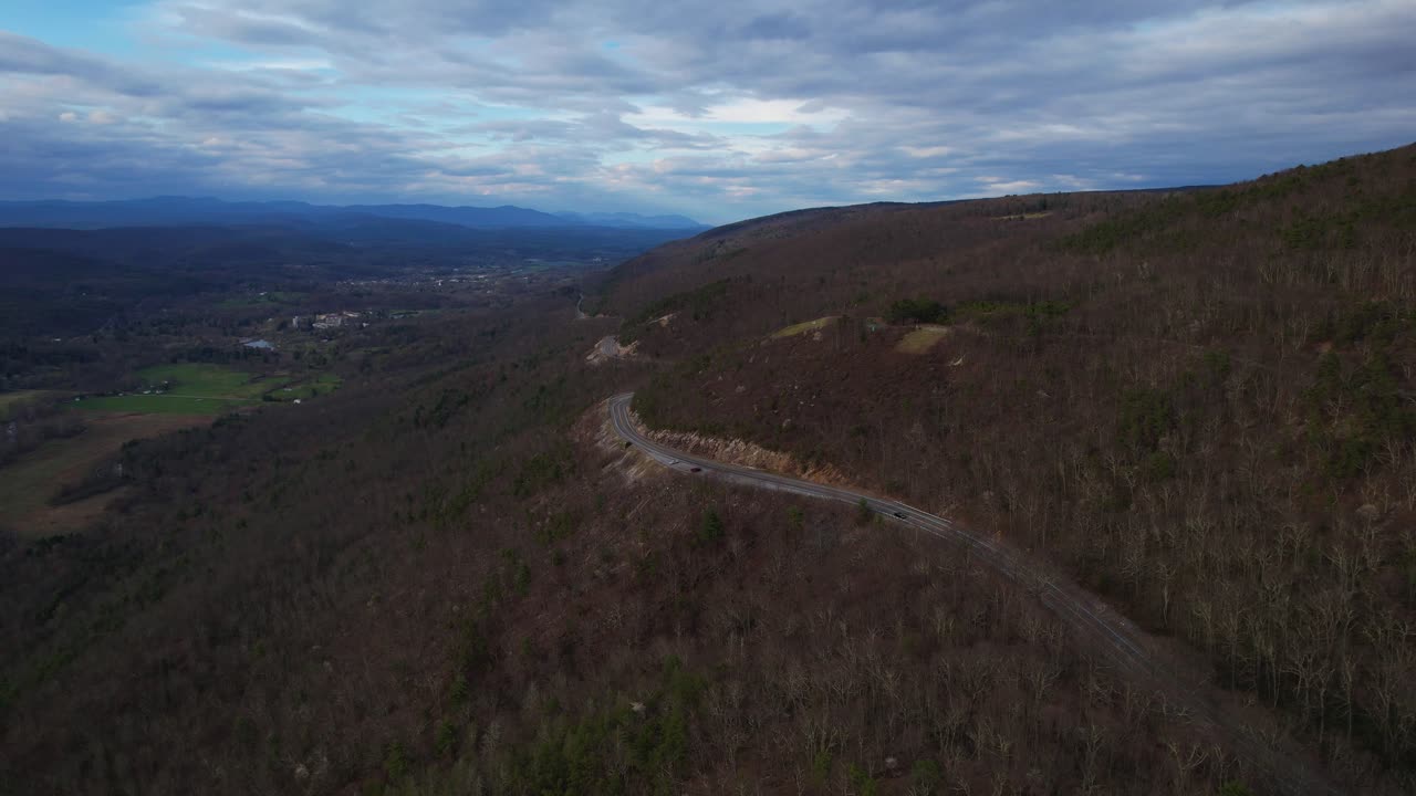 Aerial drone view of a scenic mountain valley highway in the Appalachian Mountains during late autumn sunset. The landscape is bare with no foliage, capturing a moody and serene late-fall atmosphere.
