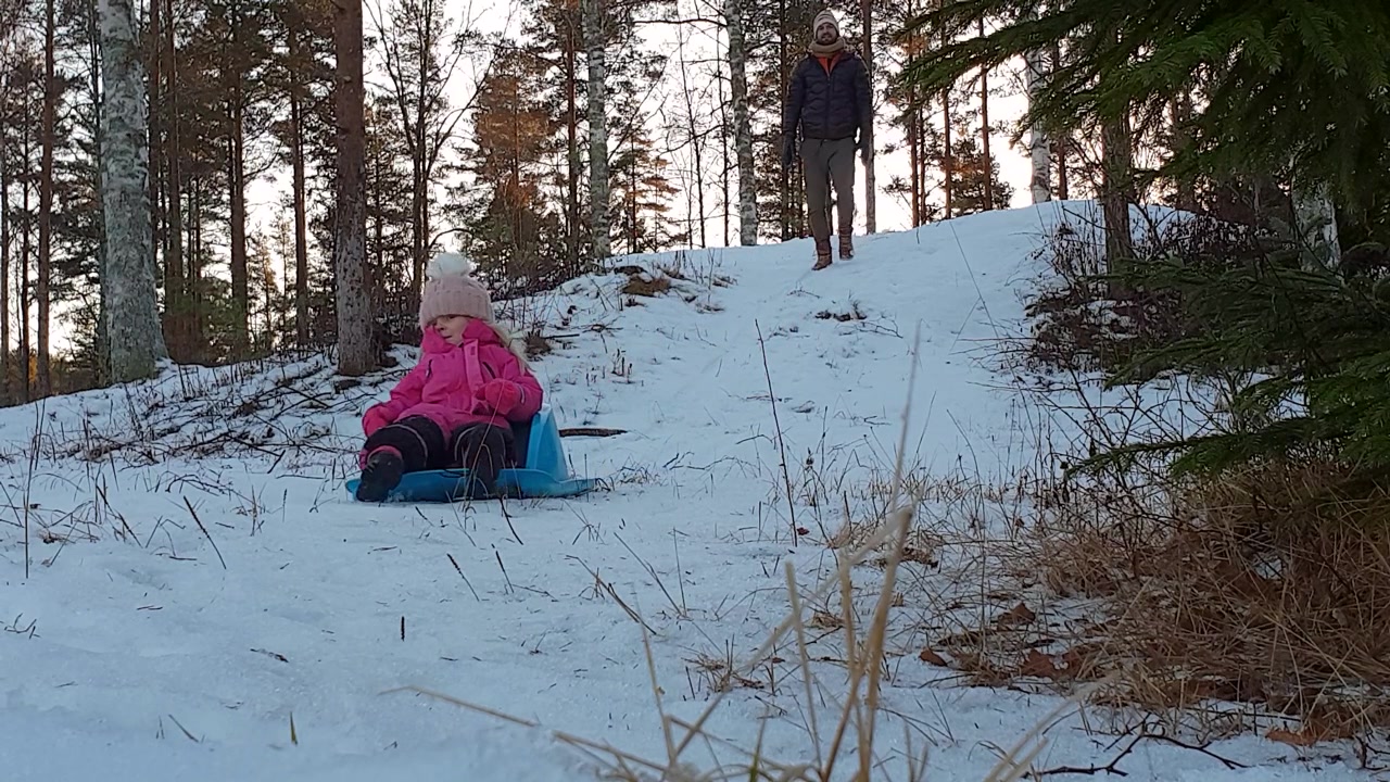 Far og datter koser seg med aking ned en bakke i snødekt natur.