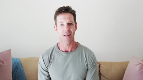 happy caucasian man sitting on sofa and making video call, talking in living room, slow motion