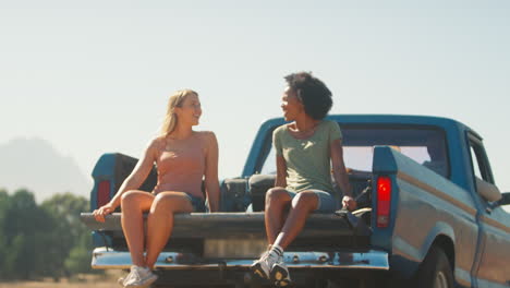 Zwei-Frauen-Fahren-Auf-Dem-Rücksitz-Eines-Pick-up-Trucks,-Während-Freunde-Auf-Einem-Roadtrip-In-Einer-Hütte-Auf-Dem-Land-Ankommen