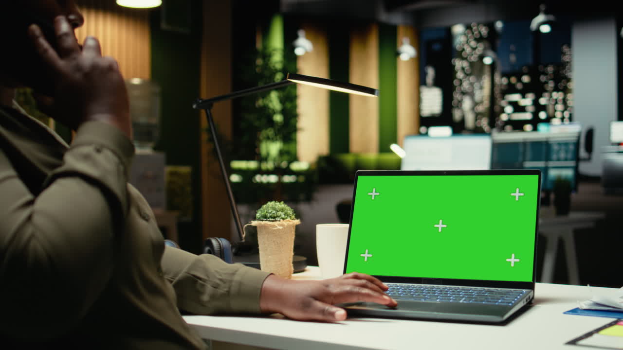 Isolated green screen on laptop next to black woman answering a phone call