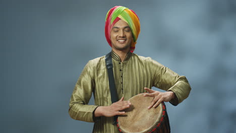 retrato de un joven indio alegre con ropa tradicional y turbante tocando un baterista y sonriendo a la cámara