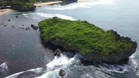 aerial view of huge coral rock overgrown with grass vegetation on the beach that crushing by the wave