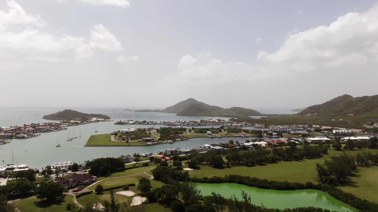 Jolly Harbor Antigua coastal view with marinas, boats, green landscapes, and hills on a cloudy day