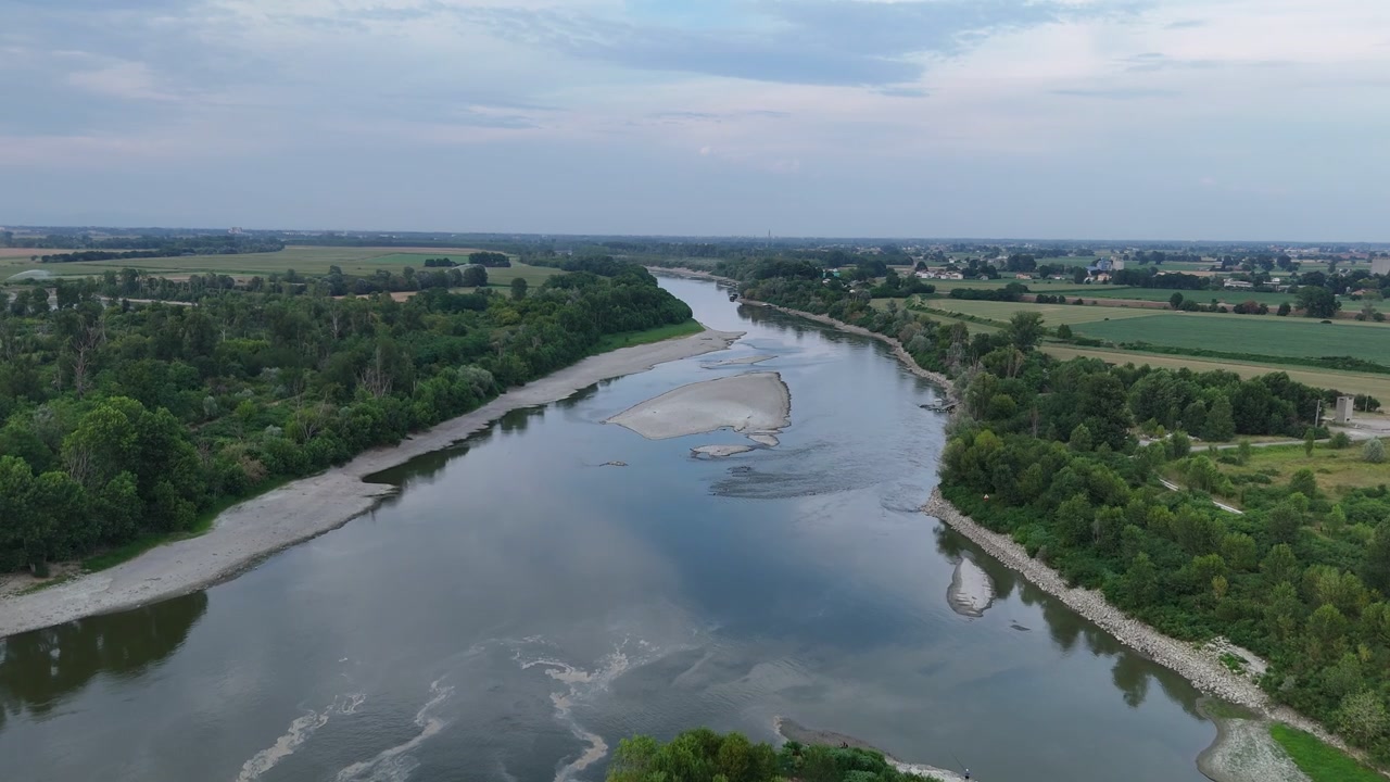 Řeka Pád blízko Isola Serafini, Monticelli d'Ongina, Piacenza, Emilia Romagna, Itálie, protéká mezi zalesněnými břehy a zemědělskou půdou s odkrytými písčinami a mělkými koryty napříč Pádskou nížinou, letecký záběr