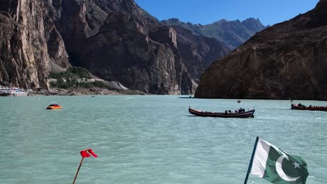 Vista-Aérea-Del-Lago-Attabad-Con-Bandera-Paquistaní-En-El-Barco-Y-La-Cordillera-A-La-Vista