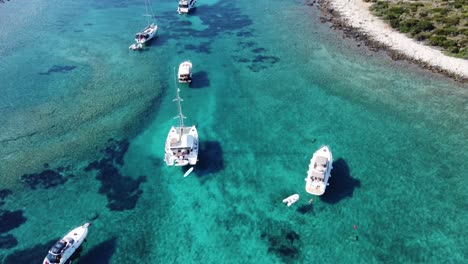 Yachts-and-cabin-cruiser-boats-of-different-types-and-sizes-anchored-in-clear-blue-water-of-Budikovac-Lagoon,-Croatia,-Aerial