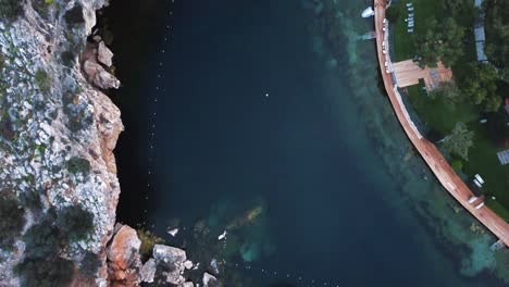 Overhead-shot-of-the-submerged-lake-Vouliagmeni-in-Athens,-Greece-with-surrounding-cliffs-and-caves-|-4K