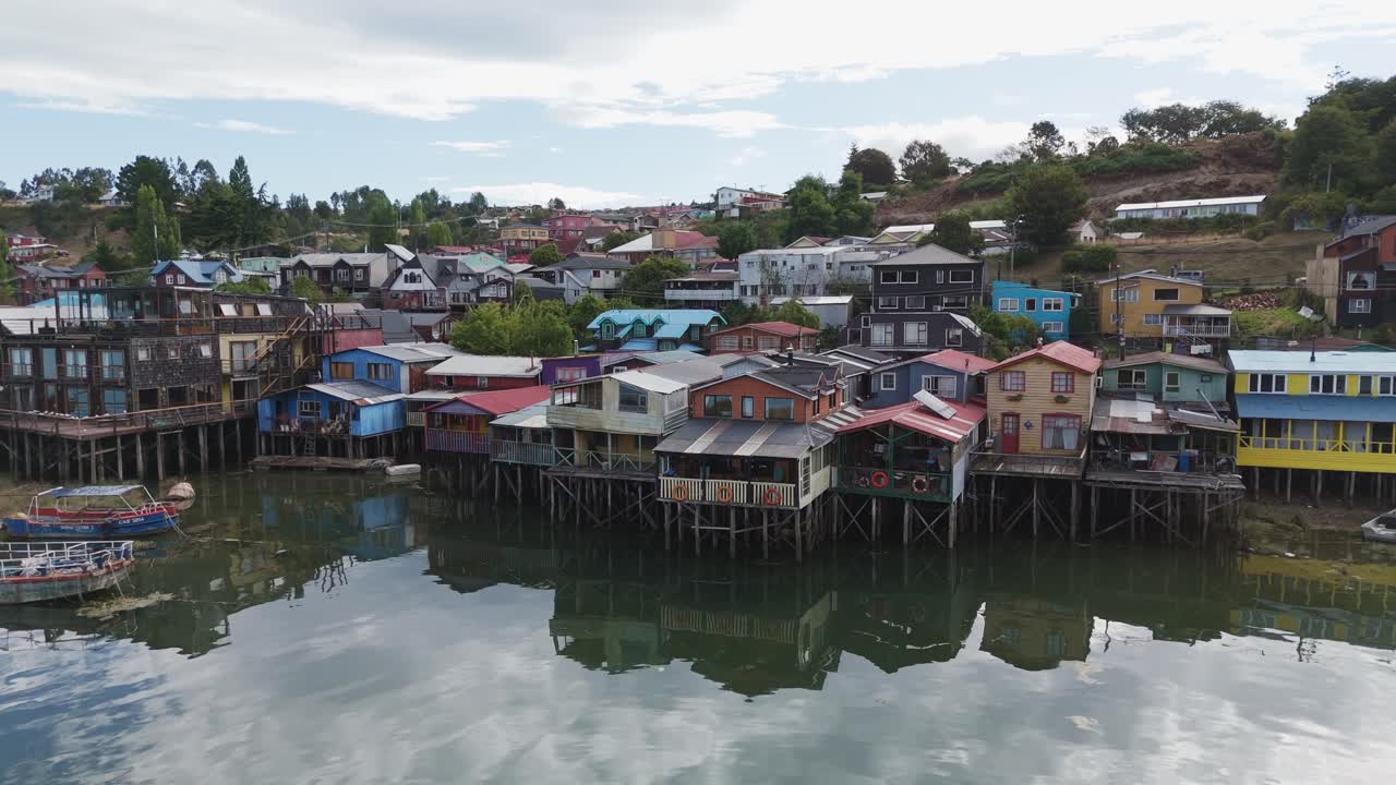 Aerial view of Vibrant stilt houses reflected on waterfront in Castro, Chiloé Island, surrounded by nature. pull back shot