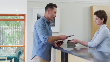 smiling caucasian man talking and paying with smartphone at reception at modern dental clinic