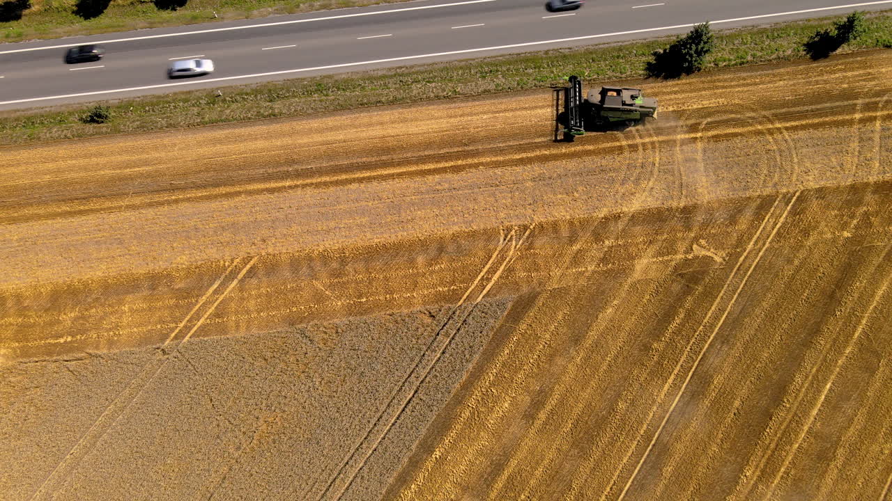자동차 운전과 함께 도로 옆 들판에서 일하는 결합 수확기의 공중 하향식 샷
