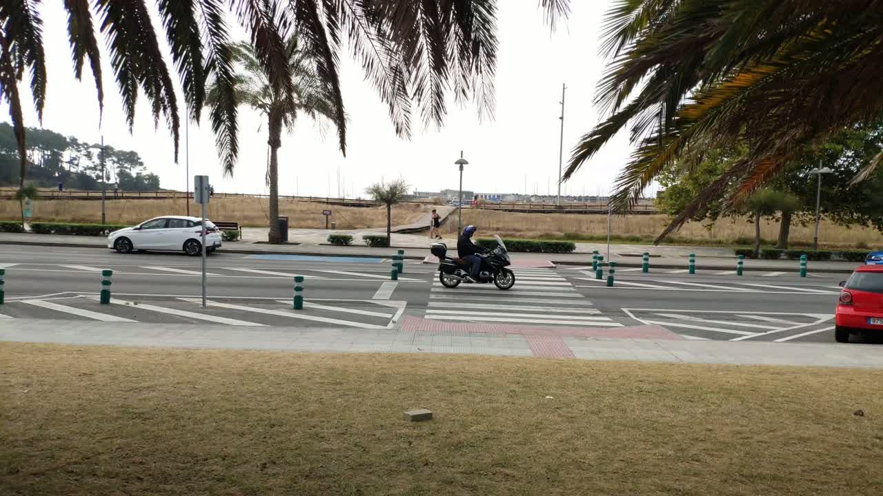 One person runs along the sidewalk and others walk in the background, crosswalk on a cloudy day, shot blocked. Porto-novo, Galicia, Spain