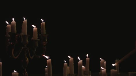 fast lighting of a group of white candles some on a candelabra lit up and running for a while