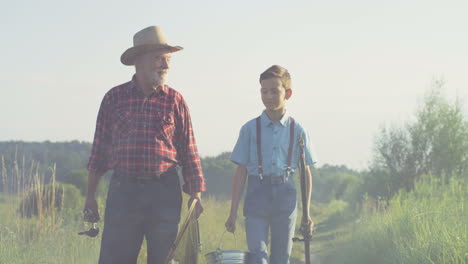 Caucasian-grandfather-and-his-little-grandson-walking-together-while-holding-fishing-rods-in-the-morning