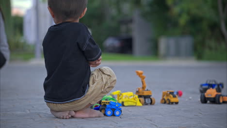 unrecognizable young mexican boy barefoot sitting on the street feeling lonely playing with his car toys with his feet dirty