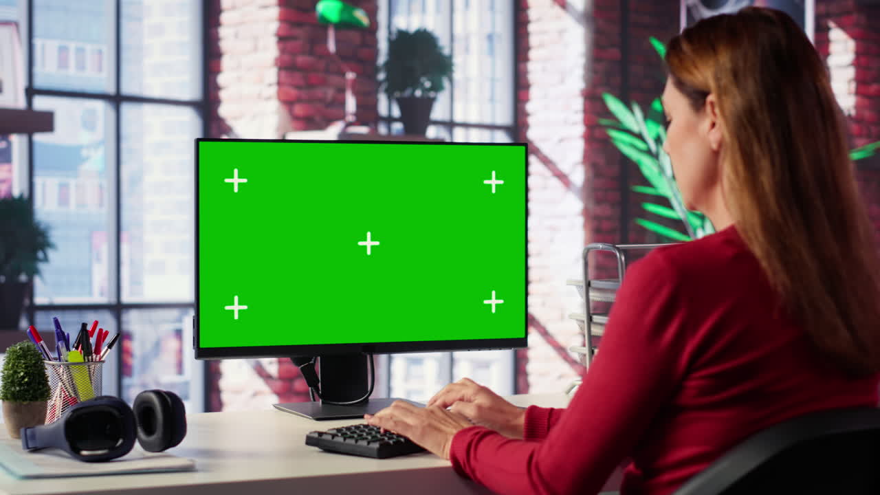 Woman working on a computer with a green screen