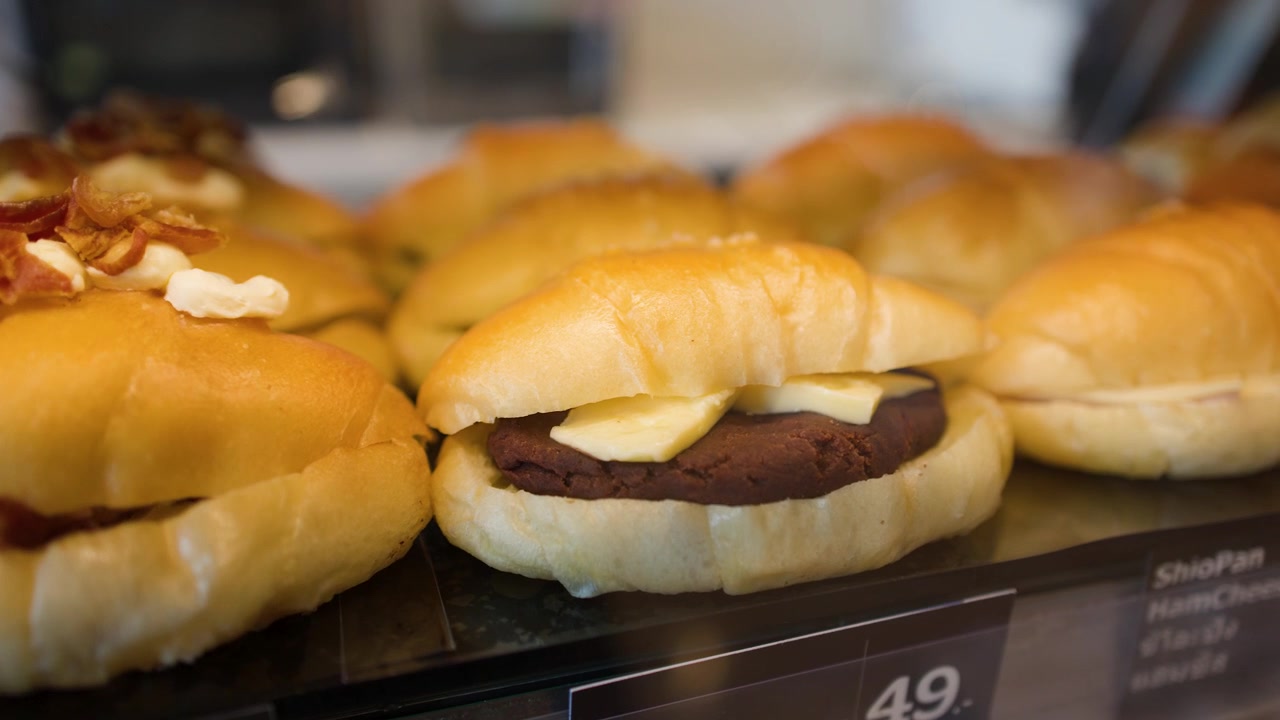明るいベーカリーのショーケースに並べられたグルメな塩パンサンドイッチをゆっくりとパンするショット。