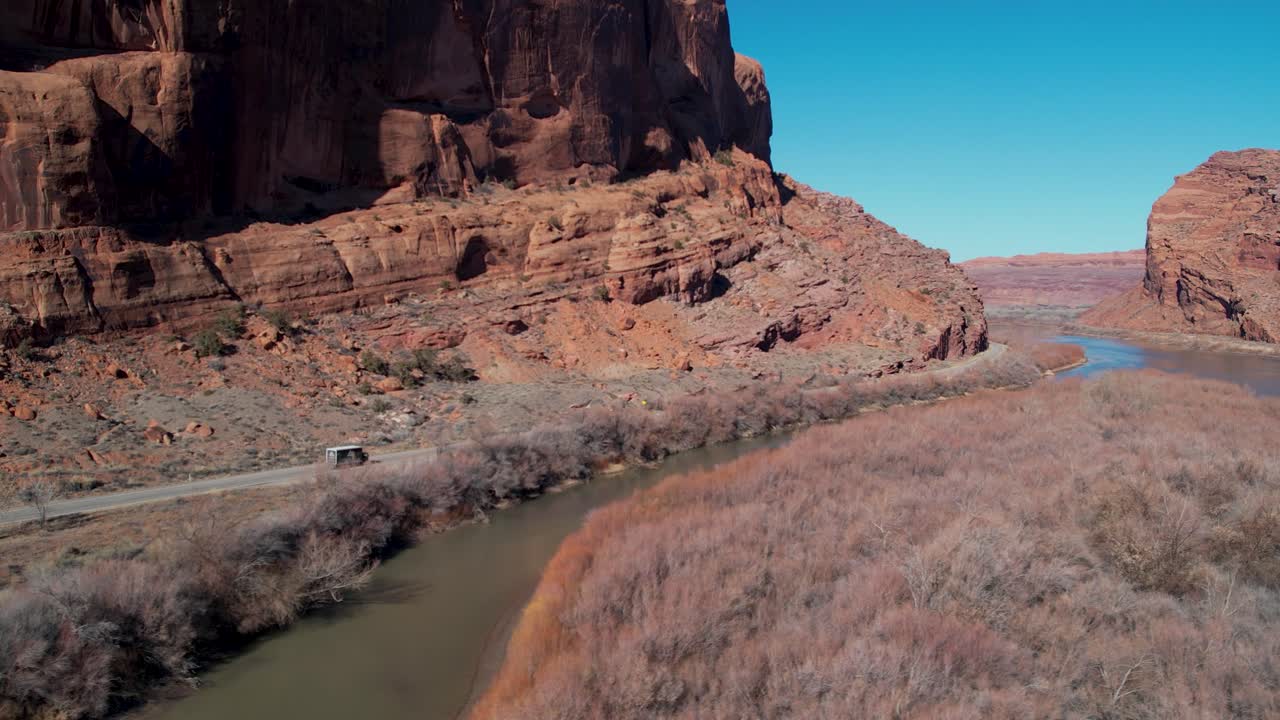 una toma de un camión de seguimiento de un avión no tripulado que conduce entre los escarpados acantilados, conocido como la "área de escalada de wall street", y el río colorado, cerca de moab, utah