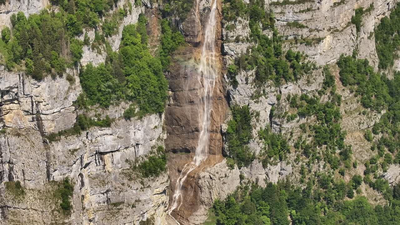thin waterfall flows along rugged cliff face in lush swiss mountain forest