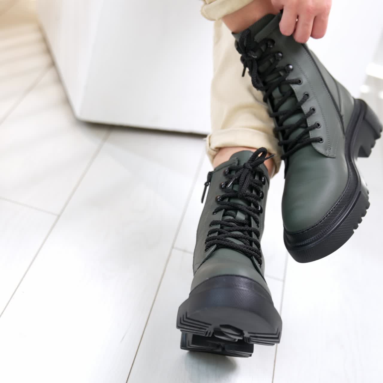 Woman sitting in studio demonstrating grey boots on tractor soles. Beautiful modern footwear at white backdrop. Close up