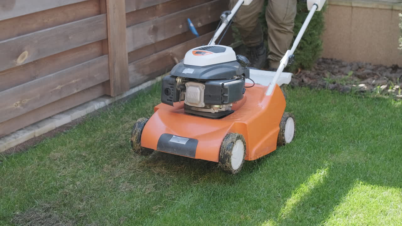 Gardener Mowing Green Grass with a Lawnmower in a Residential Backyard
