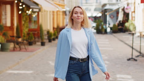 Rear-view-of-young-blonde-woman-tourist-walking-through-street-outdoors-looking-at-camera-smiling