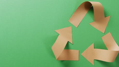 Close-up-of-recycling-symbol-of-paper-arrows-on-green-background,-with-copy-space