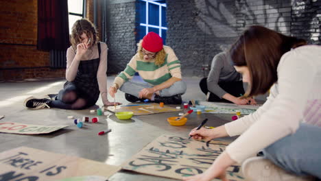 jóvenes activistas ambientales pintando carteles sentados en el suelo