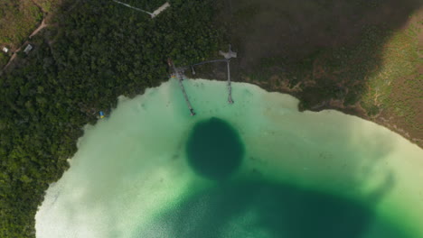 Vista-Aérea-De-Arriba-Hacia-Abajo-De-Un-Lago-Colorido-Rodeado-De-Bosque.-Sombra-De-Nubes-En-Movimiento-Atravesando-Imágenes.-Laguna-Kaan-Luum,-Tulum,-Yucatán,-México