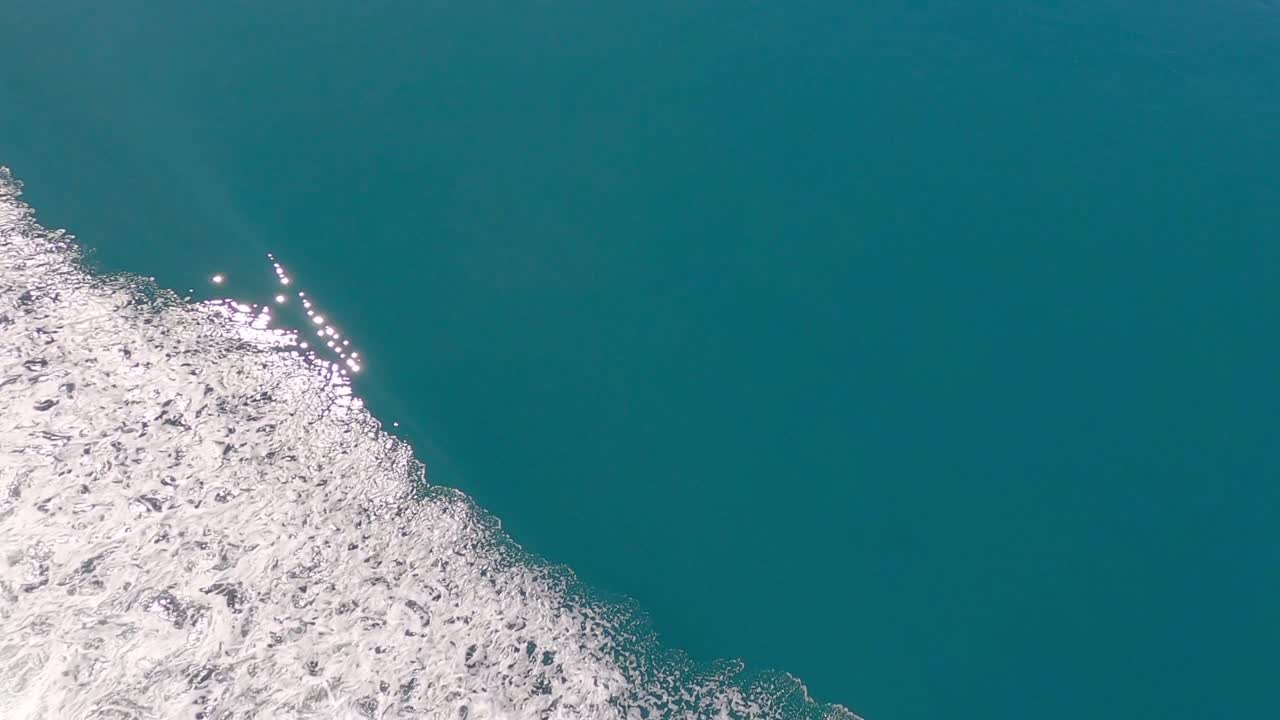 Sunshine sparkles onto beautiful turquoise-colored sea beside boat's wake - Tory Channel, South Island